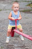 stock photo of teeter  - Smiling boy sitting on teeter on the playground on cloudy summer day - JPG 