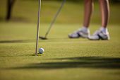 picture of golf  - Closeup of a golf ball about to go into a hole with a golfer in the background - JPG 