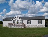 pic of home  - Gray trailer home with stone foundation or skirting and shutters in front of a beautiful sky - JPG 