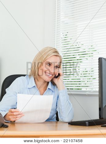Picture or Photo of Businesswoman smiling at screen while phoning and holding a paper in her office