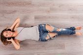 stock photo of headphones  - Beautiful caucasian woman listening music with headphones lying on the wooden floor - JPG 