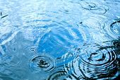 pic of ripple  - Rain drops rippling in a puddle with blue sky reflection - JPG 