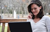 foto of technology concept  - Young woman sitting on bench in park talking on cell phone and using laptop - JPG 