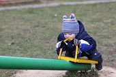 pic of seesaw  - Toddler is biting iron handle of seesaw in autumn - JPG 