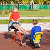 stock photo of seesaw  - Boys playing on a seesaw on a playground in a sunny day - JPG 