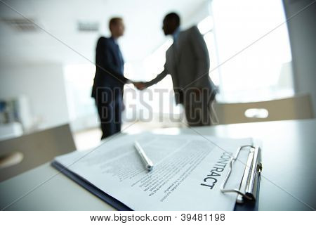 Picture or Photo of Image of business contract on background of two employees handshaking