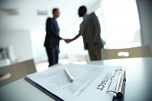picture of group  - Image of business contract on background of two employees handshaking - JPG 