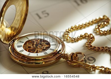 Picture or Photo of Close up of a gold pocket watch on a calendar in sunlight