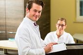 picture of receptionist  - Doctor or dentist with white coat and receptionist standing in a he gives her a clipboard - JPG 