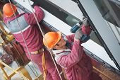stock photo of buildings  - Two builders worker installing glass windows on facade of business building - JPG 