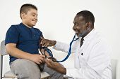 stock photo of pressure  - Happy African American male doctor checking blood pressure of a boy in clinic - JPG 