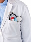 stock photo of stethoscope  - Doctor standing with stethoscope thermometer and pens inside pocket - JPG 
