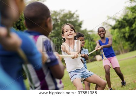 Picture or Photo of Children and recreation group of happy multiethnic school kids playing tug-of-war with rope in city park. Summer camp fun