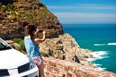 stock photo of ocean  - Tourist woman taking a photograph of scenic ocean mountain road chapmans peak in cape town south africa with rental car - JPG 