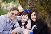 pic of cerebral  - Happy disabled boy with cerebral palsy in wheelchair surrounded by father and older sister laughing - JPG 