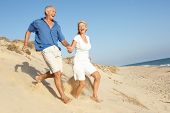 pic of holidays  - Senior Couple Enjoying Beach Holiday Running Down Dune - JPG 