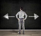 stock photo of business concept  - young business man in front of a concrete wall showing two arrows - JPG 